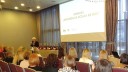 Zdjęcie przedstawia panią Dyrektor WUP w Białymstoku witająca przybyłych uczestników konferencji, siedzących przodem,  w tle widać napis prezentacji „Konkurs Organizacja ucząca się 2022”